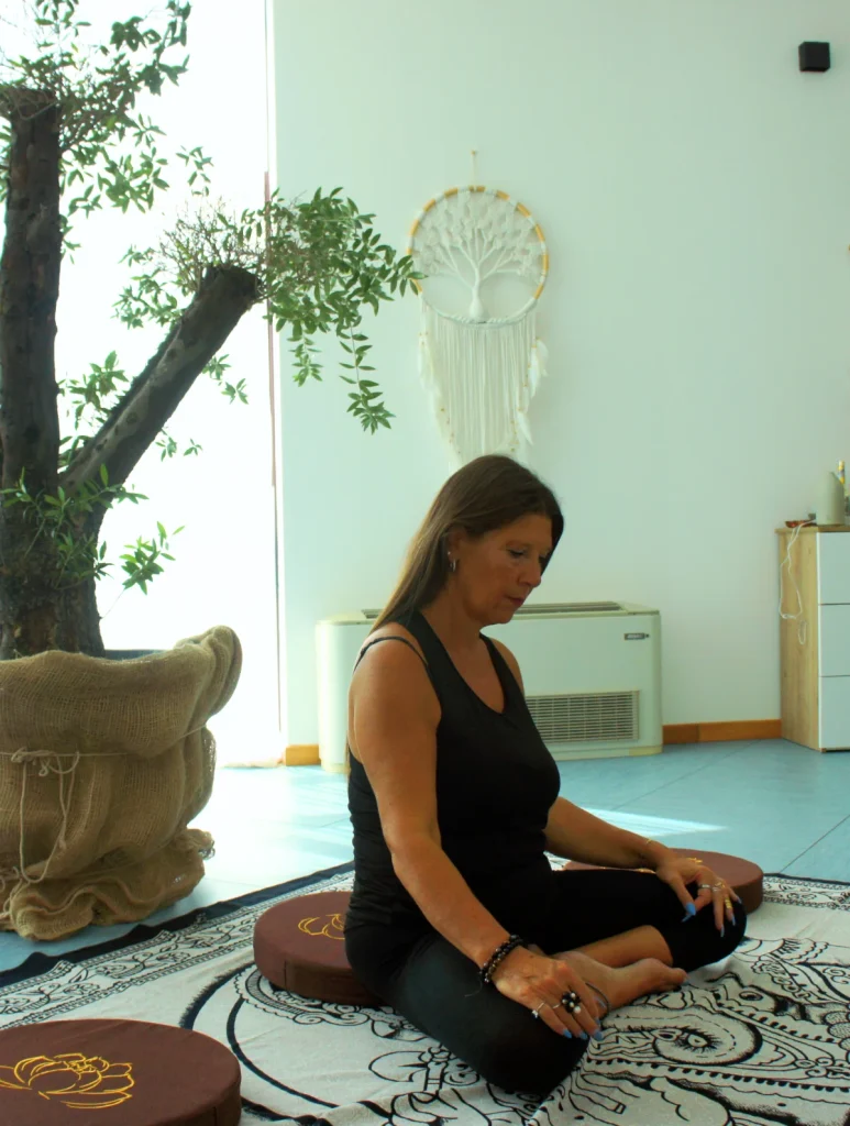 Glenda seduta in meditazione sul tappeto della shala, accanto a un ulivo in vaso