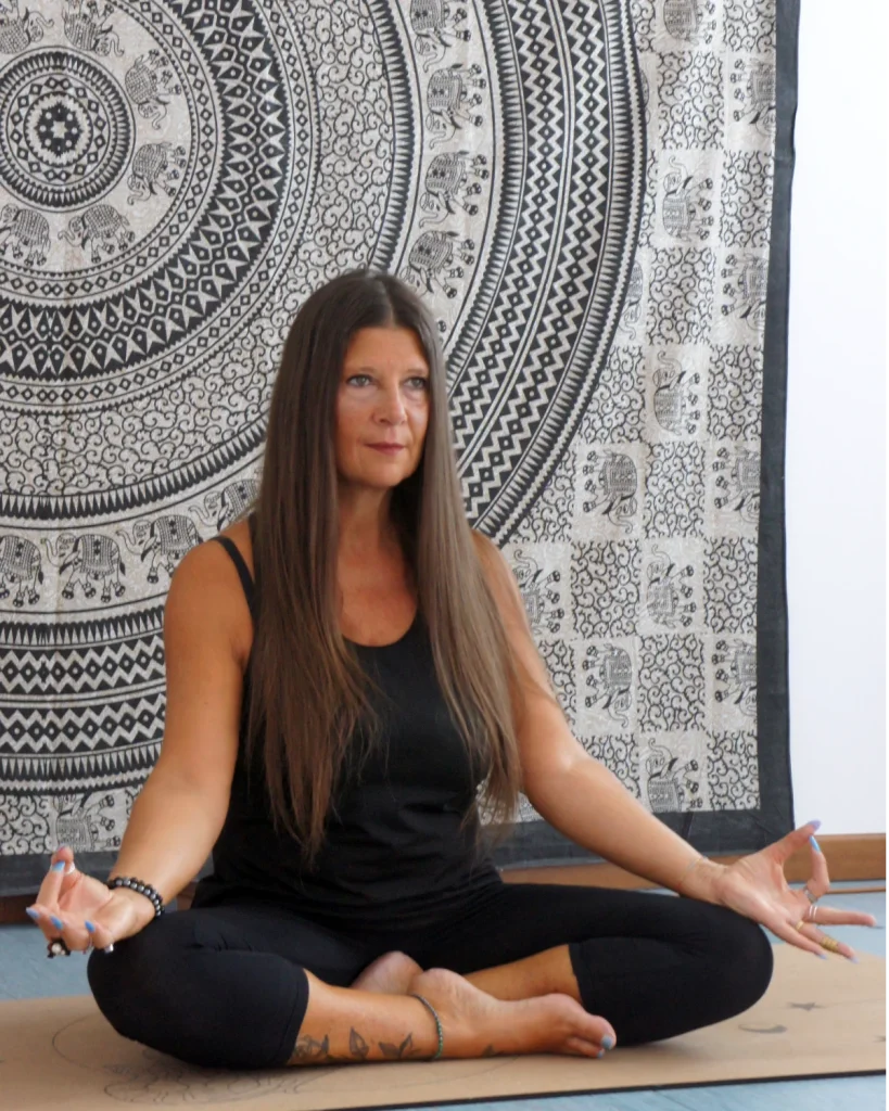 Glenda Premadevi Stradiotto seduta a gambe incrociate davanti a un telo con mandala, insegnante di yoga e fondatrice della Premadevi Shala