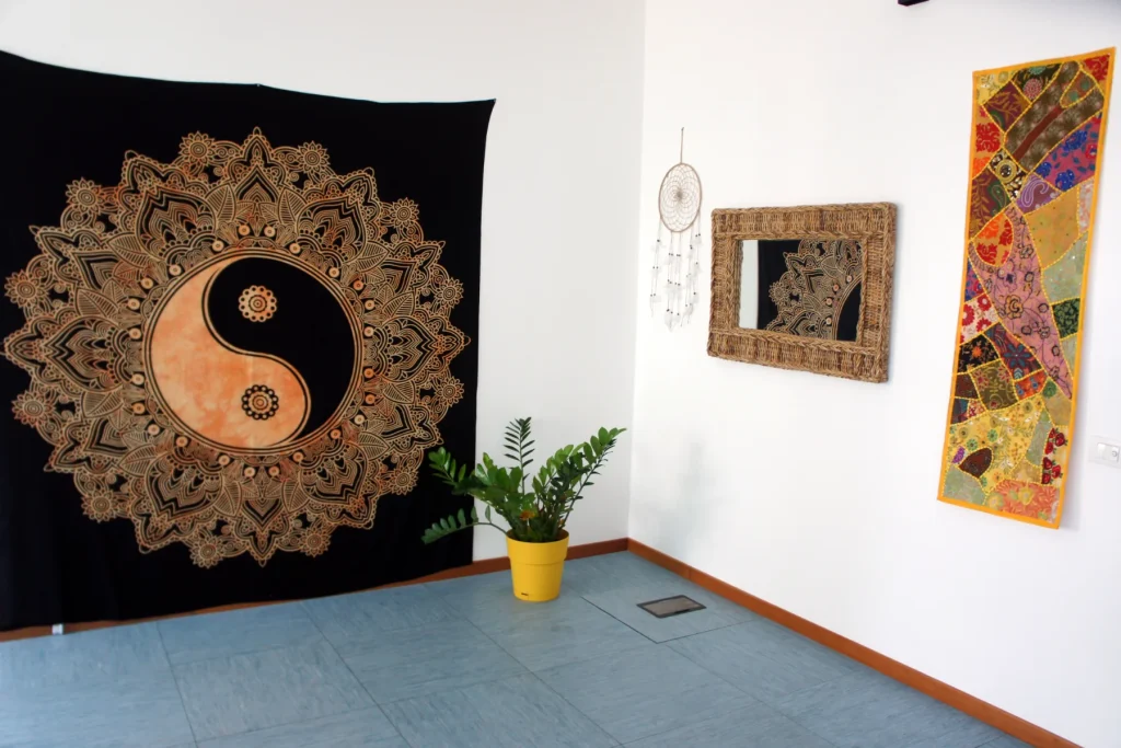 Grande mandala dorato su tessuto scuro alla parete, con specchio intagliato e pianta in vaso