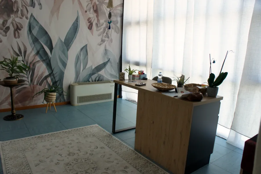 Bancone della reception in legno chiaro con piante e oggetti, davanti alla parete decorata con un grande motivo floreale